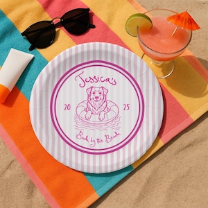May include: A round paper plate with pink and white stripes. The plate features a pink circular design with a dog in a floatie, the text "Jessica's", "20", "25", and "Back by the Beach". Sunglasses, sunscreen, and a cocktail are also visible.