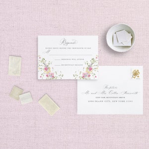 May include: A white RSVP card with floral border and text that reads "Response" and "Kindly reply before the thirteenth of May". The card has two lines for guests to indicate if they will attend or regretfully decline. The card is next to a white envelope with a handwritten address that reads "The future Mr and Mrs Collin Starworth 1229 Oak Mountain Drive Long Island City, New York 11101".