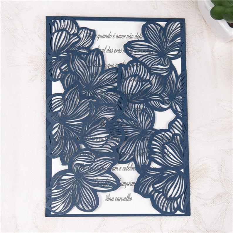 May include: A navy blue laser cut wedding invitation with a floral design. The text on the invitation reads "quando &eacute; amor n&atilde;o def al das eras que ex am e celebre umprim Ana carvalho".