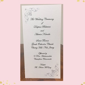 May include: A wedding ceremony program for Despina Belsemes and Asterios Karailis at Saint Thomas Greek Orthodox Church in Cherry Hill, New Jersey. The ceremony was officiated by V. Rev. Archimandrite Christoforos Othonomidis. The program features a decorative floral design.