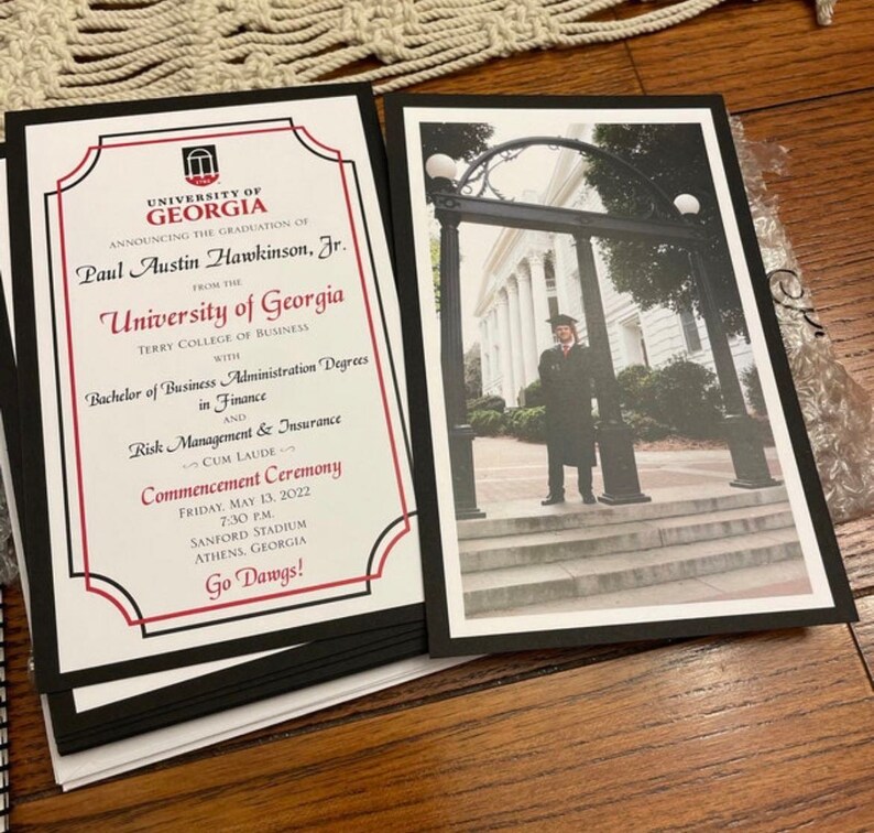 May include: A stack of graduation announcements from the University of Georgia, featuring a photo of a graduate and text announcing the commencement ceremony. The announcements have a black border and include the text "Go Dawgs!"