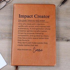 May include: A brown leather journal with the words "Impact Creator" and a definition printed on the cover. The definition describes a person who leads with intention and inspires with authenticity. The journal is personalized with the name "Carrie".