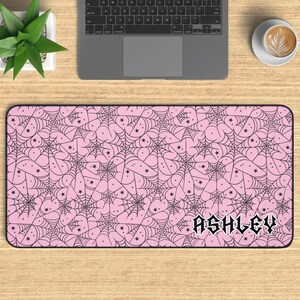 May include: Pink mouse pad with a black spiderweb pattern and stars. The name "ASHLEY" is written in black gothic font at the bottom of the mouse pad.