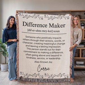 May include: A woven throw blanket with a white background and black text. The text defines the word "Difference Maker" and includes the definition: "Someone who positively impacts others through their actions, words, or character, creating meaningful change and leaving a lasting impression. This person stands out for their commitment to making a difference, often going above and beyond in kindness, service, or leadership." The text also includes the phrase "Also Known As:" followed by the name "Carrie".