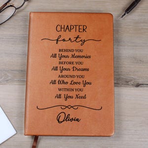 Peut inclure: Un journal en cuir marron avec les mots "CHAPTER forty" et un texte inspirant. Le journal est personnalisé avec le nom "Olivia" en bas. Un signet est visible.