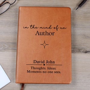 May include: A brown leather journal with the text "in the mind of an Author" and the name "David John". The journal also has the quote "Thoughts. Ideas. Moments no one sees."