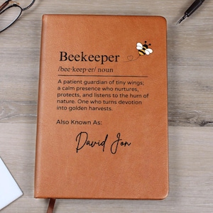 May include: A brown leather journal with the word "Beekeeper" and its definition printed on the cover. A small bee illustration is in the upper right corner. The name "David Jon" is printed at the bottom.