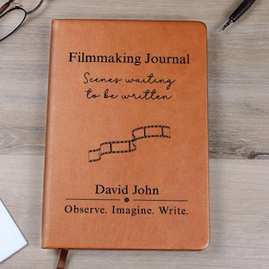 Puede incluir: Un diario de cine de cuero marrón con texto en relieve y un gráfico de tira de película. La portada dice "Escenas esperando ser escritas" y "Observa. Imagina. Escribe."