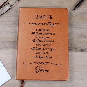 May include: A tan leather journal with the words "CHAPTER seventy" and inspirational text. The journal is personalized with the name "Olivia" at the bottom. A pen and glasses are visible in the background.