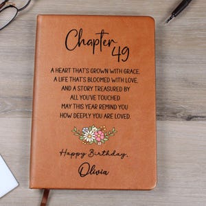 May include: A brown leather journal with the text "Chapter 49" and a floral design. The journal includes the text "A HEART THAT'S GROWN WITH GRACE...Happy Birthday, Olivia."