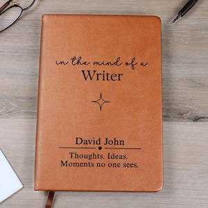 May include: A brown leather journal with the text "in the mind of a Writer" and the name "David John". The journal also has the text "Thoughts. Ideas. Moments no one sees."