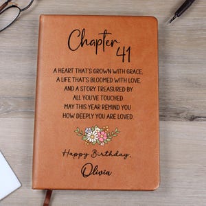 Puede incluir: Un diario de cuero marrón con el texto "Chapter 41" y un diseño floral. El diario incluye el texto "Happy Birthday, Olivia" y un mensaje sincero. Un regalo de cumpleaños reflexivo.