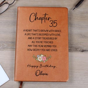 May include: A brown leather-bound journal with the words "Chapter 35" in elegant script. The cover includes a floral design and the text "Happy Birthday, Olivia," along with a heartfelt message. A perfect gift.