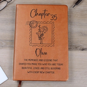 May include: A brown leather journal with the text "Chapter 35" and the name "Olivia" engraved on the cover. A floral stamp design is also featured. The journal includes the quote: "THE MEMORIES AND LESSONS THAT SHAPED YOU MADE YOU WHO YOU ARE TODAY. BEAUTIFUL, LOVED. AND STILL BLOOMING WITH EVERY NEW CHAPTER."