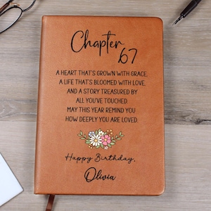 May include: A brown leather journal with the words "Chapter 67" in elegant script. The cover includes a floral design and the text "Happy Birthday, Olivia," along with a heartfelt message.