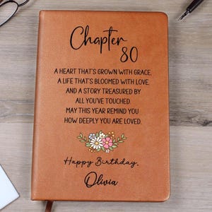 May include: A brown leather-bound journal with the text "Chapter 80" and a floral design. The journal includes the message "Happy Birthday, Olivia" and a heartfelt poem about life and love.