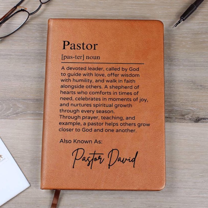 Puede incluir: Un diario encuadernado en cuero marr&oacute;n con la palabra "Pastor" definida como un l&iacute;der devoto llamado por Dios para guiar con amor, ofrecer sabidur&iacute;a y caminar en la fe junto a los dem&aacute;s. El diario tambi&eacute;n incluye el texto "Tambi&eacute;n conocido como: Pastor David".
