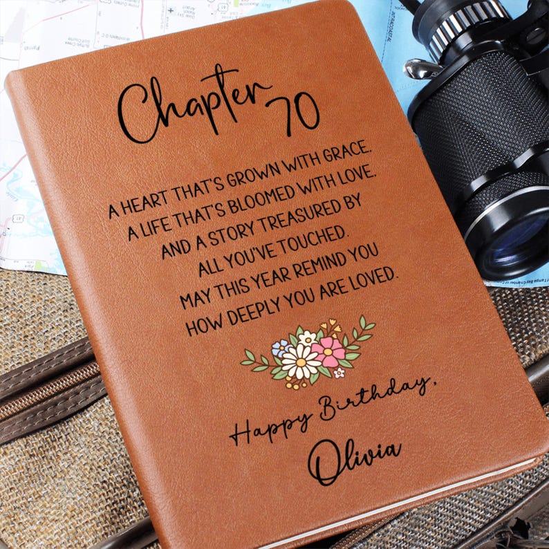 May include: A brown leather journal with the words "Chapter 70" and a floral design. The journal has a personalized message that reads "Happy Birthday, Olivia."