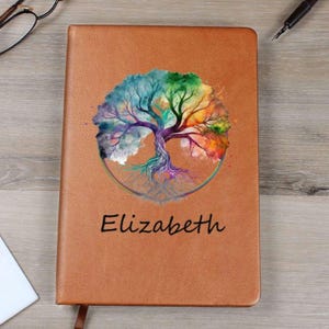Könnte beinhalten: Ein braunes Lederjournal mit einem farbenfrohen Lebensbaum-Design und dem Namen "Elizabeth" auf der Vorderseite.