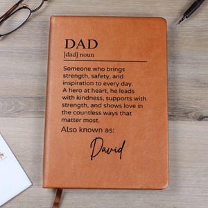 May include: A brown leather journal with the word "DAD" defined as "Someone who brings strength, safety, and inspiration to every day. A hero at heart, he leads with kindness, supports with strength, and shows love in the countless ways that matter most."  The text "Also known as: David" is also included.