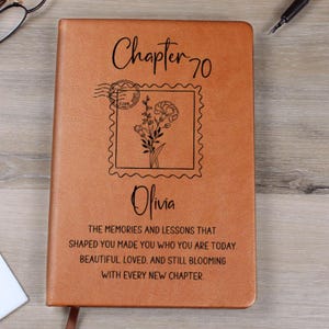 May include: A brown leather journal with the text "Chapter 70" and the name "Olivia" in elegant script. A floral stamp design is centered on the cover. The journal includes inspirational text about memories and lessons.