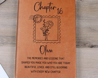 Puede incluir: Un diario de cuero marrón con el texto "Chapter 16" y el nombre "Olivia" grabados en la portada. Un diseño floral está dentro de una ilustración de sello postal. El diario también tiene una cita inspiradora.