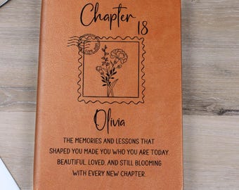 Puede incluir: Un diario de cuero marrón con el texto "Chapter 18" y el nombre "Olivia" grabado en la portada. La portada también presenta un diseño floral dentro de un borde de sello postal y texto inspirador.