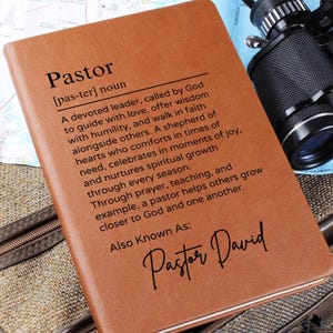 Puede incluir: Un diario de cuero marr&oacute;n con la palabra "Pastor" definida como un l&iacute;der devoto llamado por Dios para guiar con amor, ofrecer sabidur&iacute;a y caminar en la fe junto a otros. El diario tambi&eacute;n incluye el texto "Tambi&eacute;n conocido como: Pastor David".