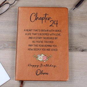 Puede incluir: Un diario de cuero marrón con la inscripción "Chapter 24" en escritura elegante. La portada presenta un diseño floral y el texto "Happy Birthday, Olivia". El diario contiene texto inspirador. Un regalo reflexivo.