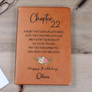 May include: A brown leather journal with the text "Chapter 22" and a floral design. The journal includes the text "A heart that's grown with grace... Happy Birthday, Olivia."