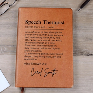 Peut inclure: Un journal en cuir marron avec les mots "Speech Therapist" et une définition du terme. Le texte comprend également les mots "Also Known As" suivis du nom "Carol Smith".