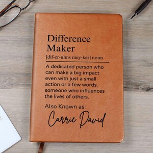Puede incluir: Un diario de cuero marrón con las palabras "Difference Maker" y una definición de la palabra. El texto también incluye las palabras "Also Known as: Carrie David".