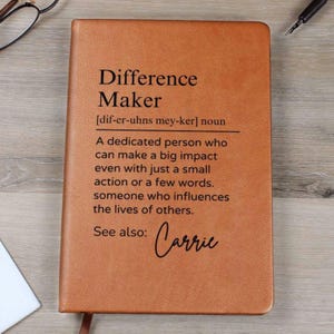 Może przedstawiać: Brązowy skórzany notes z napisem "Difference Maker" i definicją tego słowa. Pod definicją widnieje imię "Carrie".