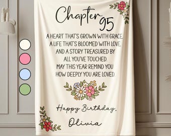 May include: Cream-coloured blanket with the text "Chapter 95" and a birthday message. Floral accents in pink, red, and white decorate the corners and centre. The blanket includes the name "Olivia".