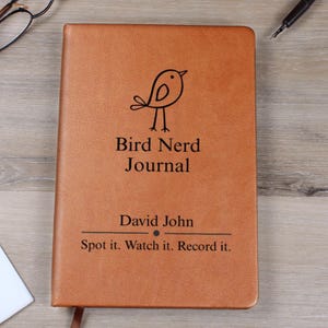 May include: A brown journal with the text "Bird Nerd Journal" and a small bird illustration. The journal also includes the name "David John" and the phrase "Spot it. Watch it. Record it."
