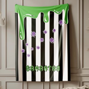 May include: A black and white striped blanket with a green slime design at the top. Purple bug illustrations are scattered across the blanket. The name "SAMANTHA" is printed in green at the bottom.