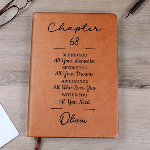 以下が含まれることがあります： 「Chapter 68」のテキストとインスピレーションを与えるフレーズが書かれた茶色の革製ジャーナル。下部には「Olivia」という名前が書かれています。ジャーナルにはリボンのブックマークが付いています。
