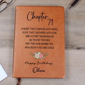 Puede incluir: Un diario de cuero marrón con el texto "Capítulo 71" y un diseño floral. El diario incluye el texto "Feliz Cumpleaños, Olivia" y un mensaje sincero. Un regalo perfecto para un cumpleaños.