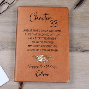 May include: A brown leather journal featuring the text "Chapter 33" and a floral design. The journal includes the text "A heart that's grown with grace..." and "Happy Birthday, Olivia."