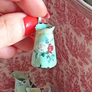 Peut inclure: Une petite cruche bleu clair d'aspect vieilli, avec une anse. La cruche est ornée de roses blanches et rouges et de feuilles vertes. La cruche a un aspect légèrement usé.