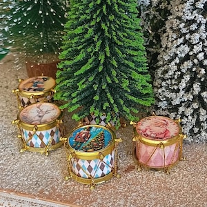 Könnte beinhalten: Vier Miniatur-Weihnachtstrommeln mit verschiedenen weihnachtlichen Designs. Die Trommeln sind mit goldenen Verzierungen verziert und haben eine Vielzahl von Farben, darunter Rot, Blau, Grün und Weiß.