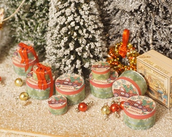 May include: Miniature Christmas gift boxes with red ribbon and festive designs. The boxes are round, with green and red accents, and feature holiday graphics. Gold and red ornaments and a dollhouse box are also present.