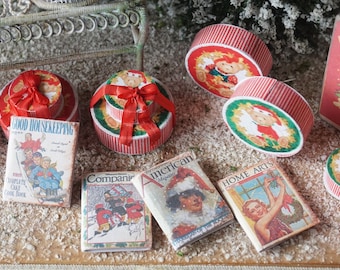 May include: Miniature Christmas-themed items, including round boxes with red and white stripes, red bows, and illustrations of a teddy bear. Also, miniature vintage magazines with titles like "Good Housekeeping" and "American Magazine".