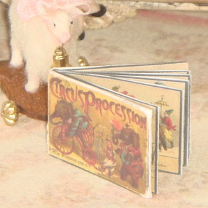 May include: A vintage children's book titled "The Circus Procession" with colourful illustrations of elephants, clowns, and a band. The book is open to reveal several pages with different scenes.
