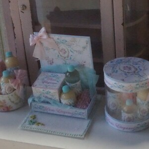 May include: A set of decorative gift boxes with a floral design. The boxes are filled with small bottles of liquid and are decorated with ribbons and bows. The boxes are on a white surface.