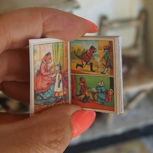 May include: A small, vintage book with colourful illustrations of cats. The book is open to a page with a cat wearing a red coat and a hat, delivering a letter to another cat.