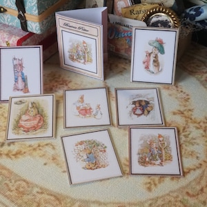 Op de afbeelding: Miniatuur illustraties van Beatrix Potter-personages, waaronder Peter Konijn, weergegeven op een patroon oppervlak. De collectie bevat ingelijste prints en een klein boekje, met gedetailleerde aquarel kunstwerken met zachte kleuren en een vintage esthetiek.