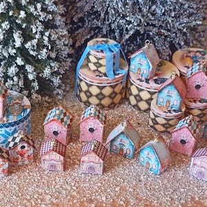 Pode incluir: Uma coleção de casas em miniatura decoradas com vários padrões e cores, incluindo rosa, azul e branco. Algumas casas têm um padrão xadrez, enquanto outras têm um design mais intrincado. As casas estão dispostas sobre uma superfície de madeira, com algumas empilhadas umas sobre as outras.