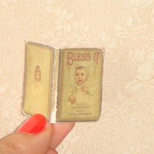 May include: A vintage book titled "Bless It" featuring a child on the cover. The book is illustrated with a child wearing a white dress and a white bonnet. The book is bound in brown paper with a gold spine.