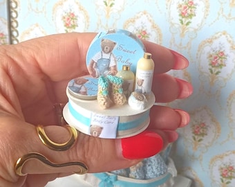 Prezent w postaci zestawu do pielęgnacji ciała dla niemowląt w domku dla lalek. Miniatura wanienki dla niemowląt Just Born w skali 1:12 do domków dla lalek. Miniatura perfum w domku dla lalek.